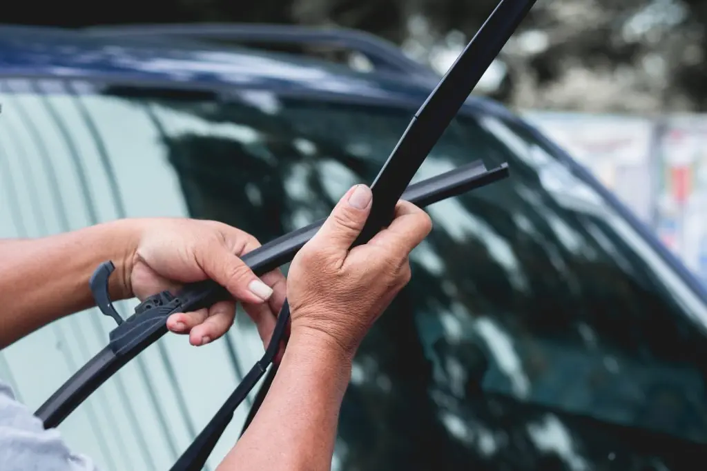 Hands installing new wiper blade on windshield as part of regular vehicle maintenance