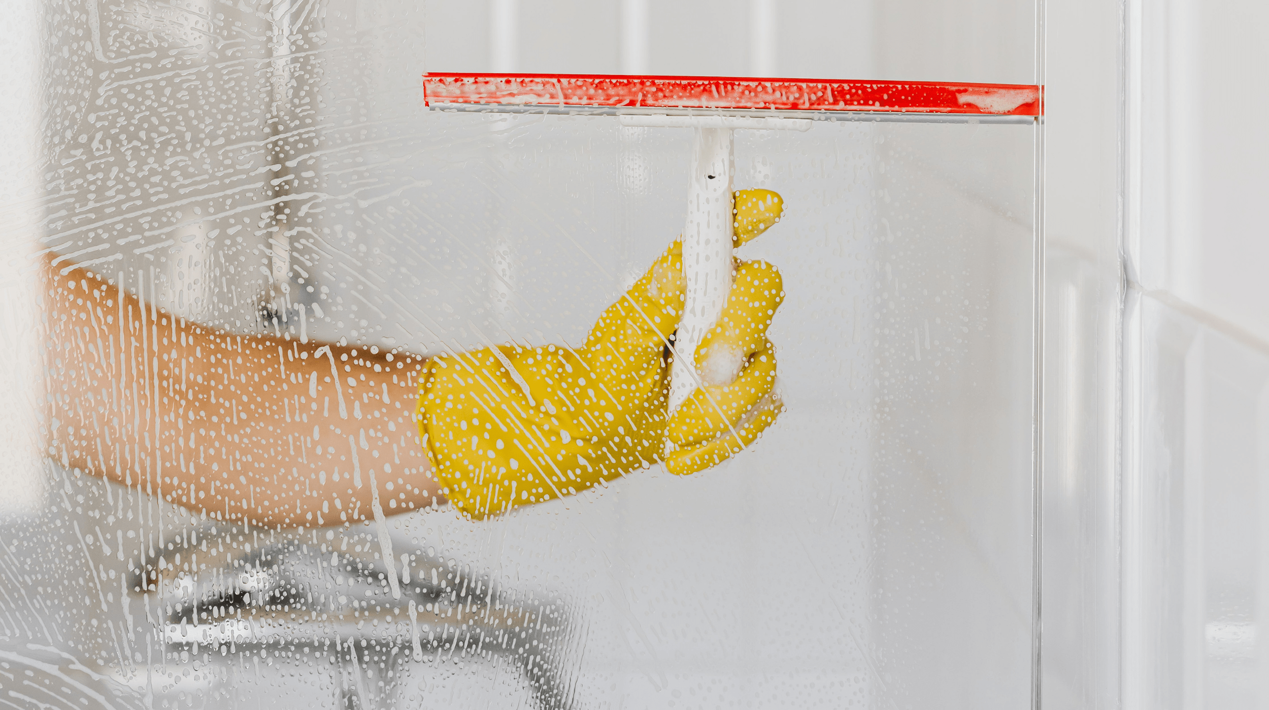 A shower glass door in the middle of being cleaned with a squeegee and gloves, highlighting best practices for cleaning shower glass.