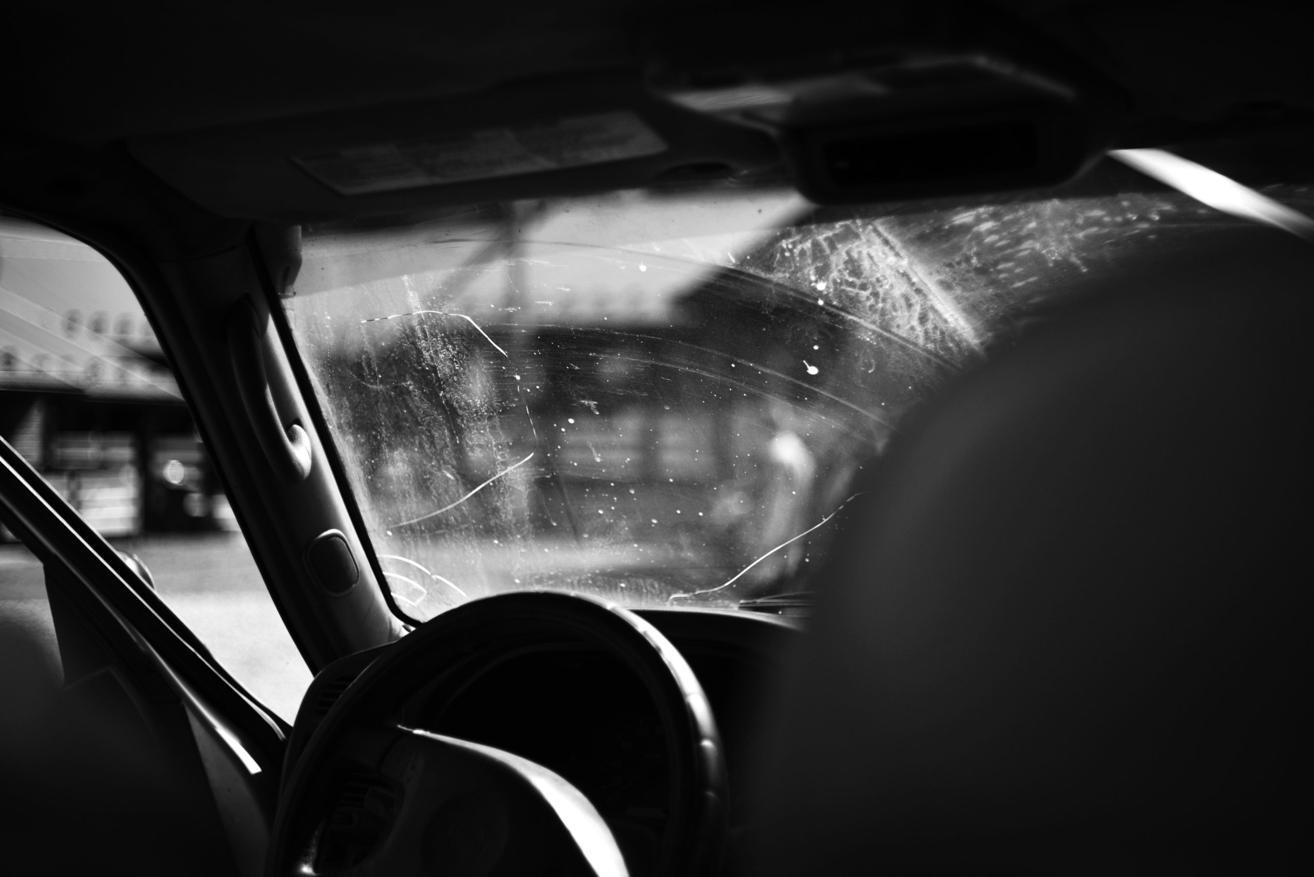 Black and white view from inside a vehicle showing a cracked windshield, highlighting damage that requires immediate repair to prevent spreading.